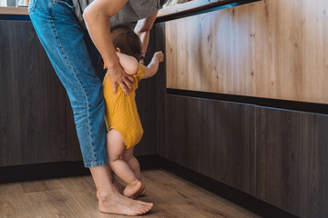 Mother picking up the angry baby standing at her feet. Mother and her baby.