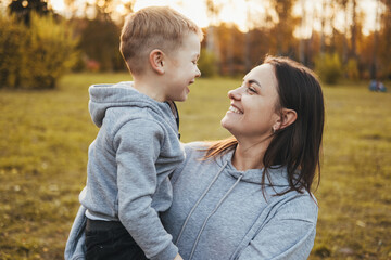 Fototapeta premium Little boy holded by his mom in the arms which is laughing. Side view. Happy family together. Happy family leisure.