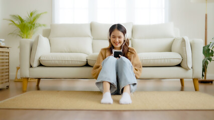 Obraz premium Happy young asian woman relaxing at home. Female smile sitting on sofa and holding mobile smartphone. Girl using video call to friend