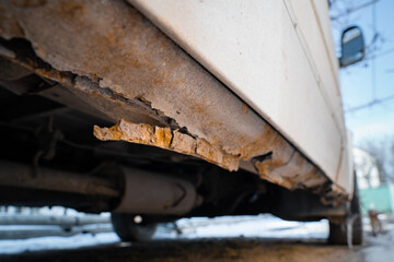 Rusted through the threshold of a white car close-up. Corrosion of the bottom of the car after winter