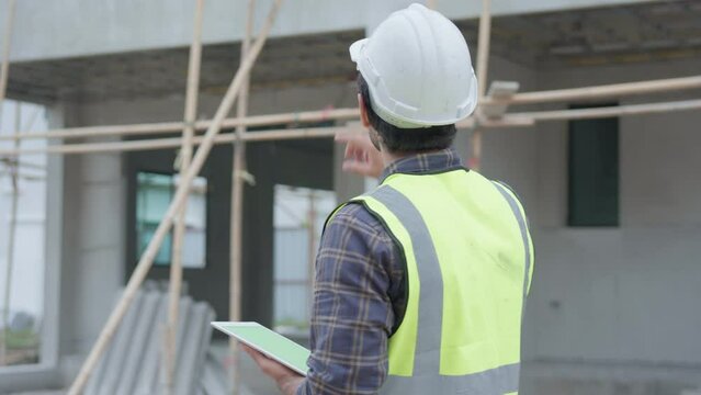 Professional male civil engineer or architect wear safety helmet. While engineer, inspector walking use tablet technology for check list building project on construction site. Real estate concept.