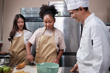 Cuisine course, senior male chef in cook uniform teaches young cooking class students to knead and...