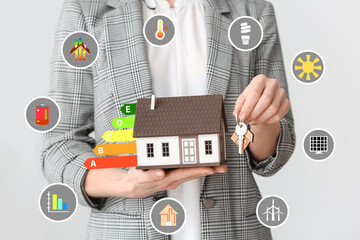 Female real estate agent with model of house and key on grey background, closeup. Concept of energy...