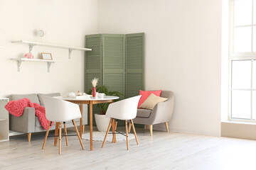Interior of light dining room with sofa, armchair, folding screen, table and chairs