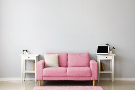 Stylish interior with pink sofa and tables near light wall