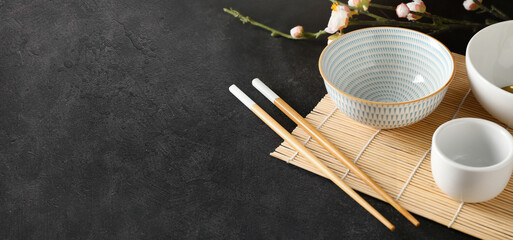 Chinese bowls with chopsticks and bamboo mat on dark background with space for text