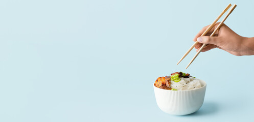 Woman eating tasty rice noodles on light blue background with space for text