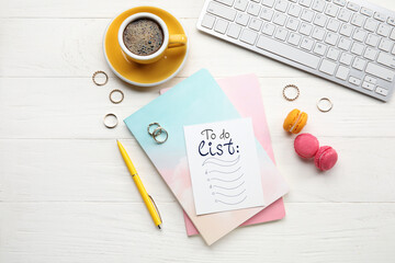 Notebook with blank to-do list, computer keyboard, coffee and macarons on white wooden background