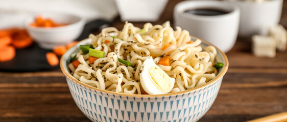 Bowl of tasty Chinese noodles with egg on wooden table, closeup