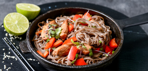 Frying pan with tasty soba noodles and meat on dark background, closeup