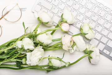 Obraz na płótnie Canvas Beautiful ranunculus flowers, keyboard and eyeglasses on light wooden background, closeup