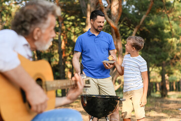 Naklejka na ściany i meble Handsome man with his little son cooking food on grill at barbecue party