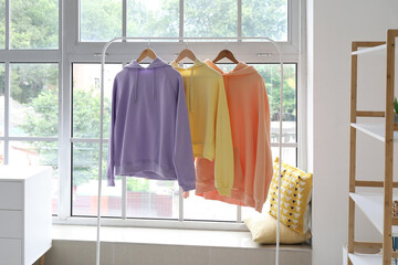 Rack with stylish hoodies near window in room