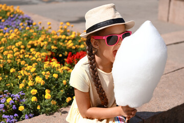 Cute little girl eating cotton candy outdoors