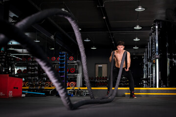 Fitness muscular man working out training with rope in functional training fitness gym is CrossFit exercise concept.