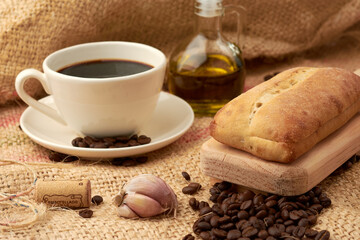 Obraz na płótnie Canvas Rustic bread placed on a cutting board, around it a cup of American-style coffee, olive oil, coffee beans and garlic, placed in a vegetable fiber sack