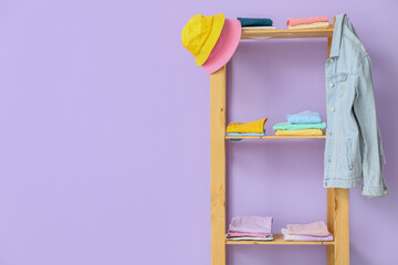 Wooden shelf unit with stylish clothes near violet wall