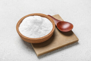 Bowl with baking soda and spoon on light background