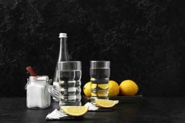 Glasses with water, baking soda and pieces of lemon on dark background