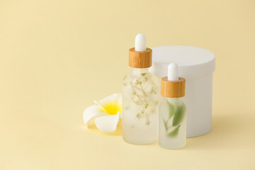 Bottles of natural serum with flower on yellow background