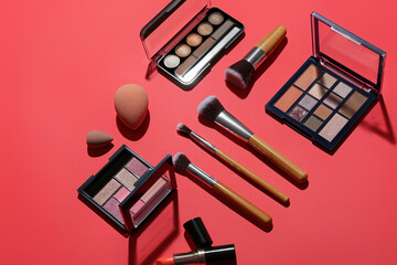 Makeup brushes with decorative cosmetics on red background