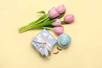 Bouquet of pink tulips, gift box, perfume bottle and female accessories on yellow background