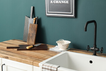 Cutting boards with knife, colander and sink on counter near green wall