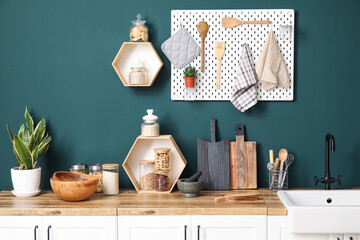 Wooden boards with kitchen utensils and sink on counters near green wall