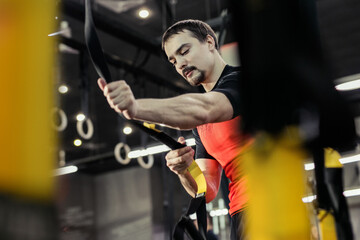 Fototapeta na wymiar Sports background. Man training with fitness straps in the gym. 