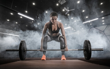 Fototapeta na wymiar Sport. Muscular women lifting deadlift in the gym with barbell. Dramatic interior with smoke.