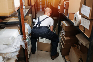 Back view of a male warehouse worker picking up a box from the floor safely