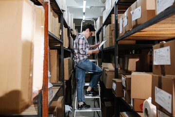 Reading female warehouse worker standing on the ladder, next to shelves