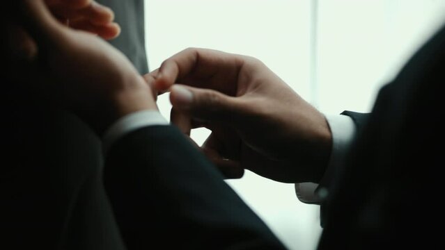 Confident businessman in classic blue suit buttoning or adjust cufflinks near window in hotel room at the morning. Handsome man wearing a nice suit on wedding day.