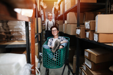 Excited warehouse workers playing with a cart, man pushes woman riding in it