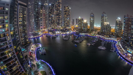 Dubai marina tallest skyscrapers and yachts in harbor aerial night timelapse.