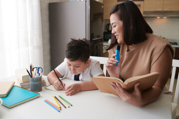 Smiling mother helping son with doing homework for school