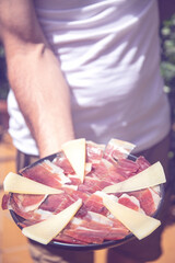 man holding plate of cured ham and cheese. close up. selective focus.