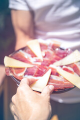 man holding plate of cured ham and cheese. close up. selective focus.