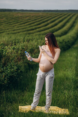 Beautiful young pregnant woman talking on the phone in nature holding a bottle of water