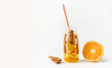 Tasty lemonade in bottle with drinking straw and ingredients: orange and cinnamon sticks at white...
