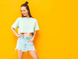 Portrait of young beautiful smiling female in trendy summer jeans skirt. carefree woman posing near yellow wall in studio. Positive model having fun indoors. Cheerful and happy