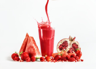Red smoothie flows in glass with splashing at white background with fruit ingredients: watermelon, pomegranate, strawberries and raspberries. Healthy refreshing drink.  Front view.