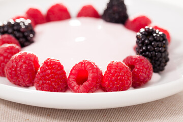 fresh raspberries and blackberries laid out on a white plate in circle with yogurt