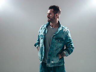 Fototapeta premium Portrait of handsome confident stylish hipster lambersexual model. Sexy man dressed in jeans jacket. Fashion male isolated on grey background in studio