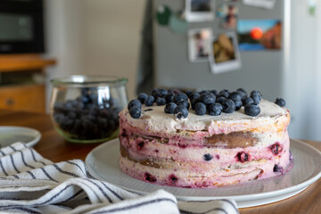 Homemade, slightly messy Victoria sponge cake with blueberries and mascarpone cream on a kitchen counter in front of a retro fridge