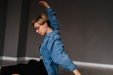 Young woman with short hair dancing on the floor indoors. Girl doing yoga exercise in studio