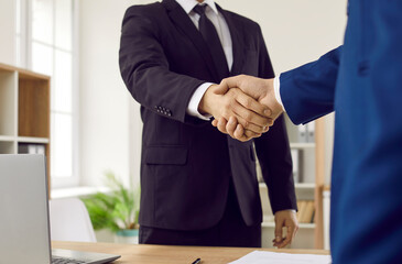 Handshake after successful consultation or negotiation between lawyer and client in office. Close up of greeting or farewell handshake of two men in formal suits. Legal concept.