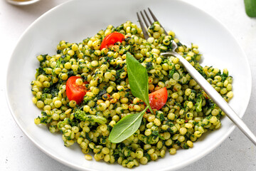 Ptitim pasta close up. Traditional Israeli pasta with spinach and broccoli, cherry tomatoes in white plate.
