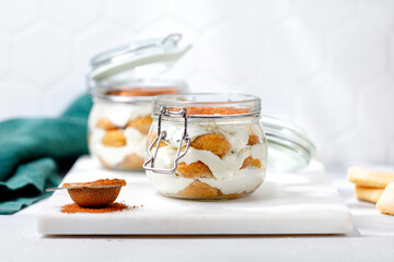 Woman's hand pours cocoa on a tiramisu dessert in a glass jar. Tiramisu cake, italian dessert.