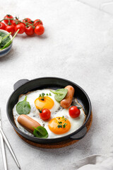Fried eggs in a small pan with tomatoes, spinach, sausages. English breakfast, keto diet. Top view, copy space.
